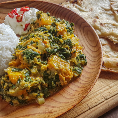 In a wooden plate, a ball of white rice next to a mixture of mallow and pumpkin and a spoonful of sour cream, next to the plate a flatbread.