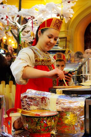 A woman in traditional Russian dress prepares Maslenitsa pancakes with a Kramoupz