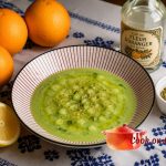 Cold cucumber salad with orange and za’atar, served on a red-and-white striped plate, placed on a white tablecloth embroidered with blue Fez stitch, surrounded by three oranges, half a lemon, a bottle of orange blossom water and a ramekin of za’atar