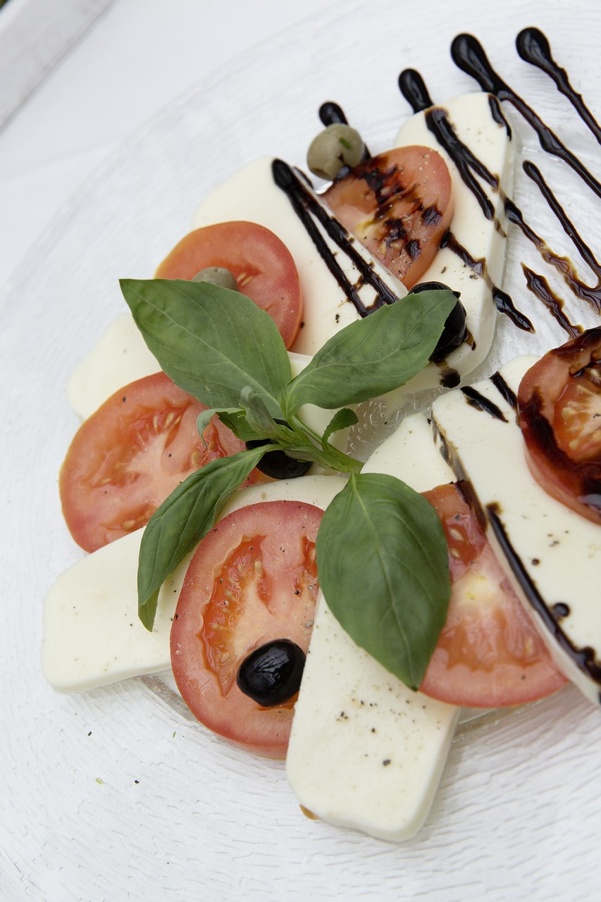 Sliced tomatoes and mozzarella with a bouquet of basil leaves, a black olive and streaks of balsamic vinegar